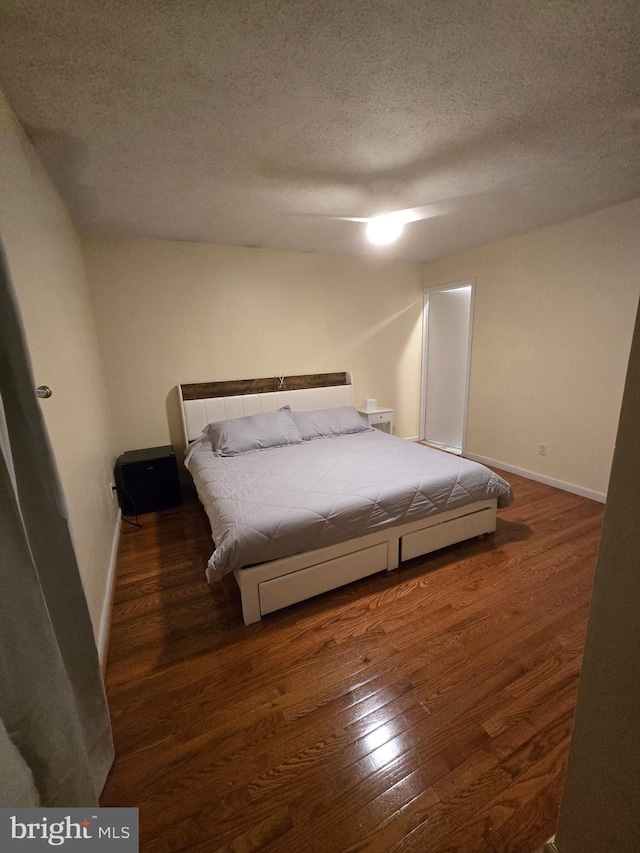 bedroom featuring a textured ceiling, baseboards, and wood finished floors