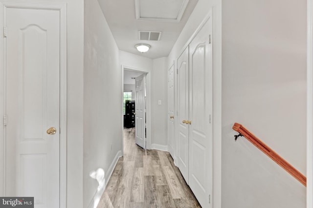 hallway featuring visible vents, light wood finished floors, and baseboards