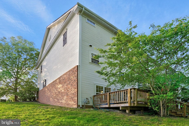 back of property featuring brick siding, a lawn, and a deck