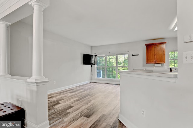 unfurnished living room with a healthy amount of sunlight, baseboards, light wood-style floors, and ornate columns