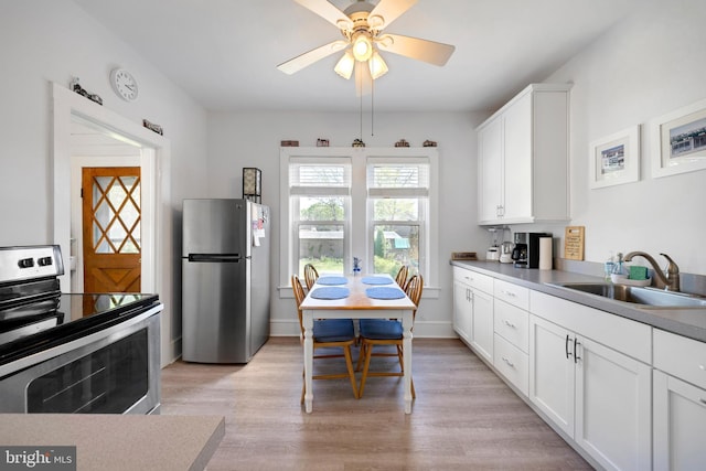 kitchen with a ceiling fan, white cabinets, a sink, light wood finished floors, and stainless steel appliances