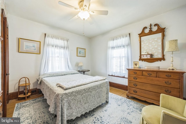 bedroom with baseboards, a ceiling fan, wood finished floors, and multiple windows
