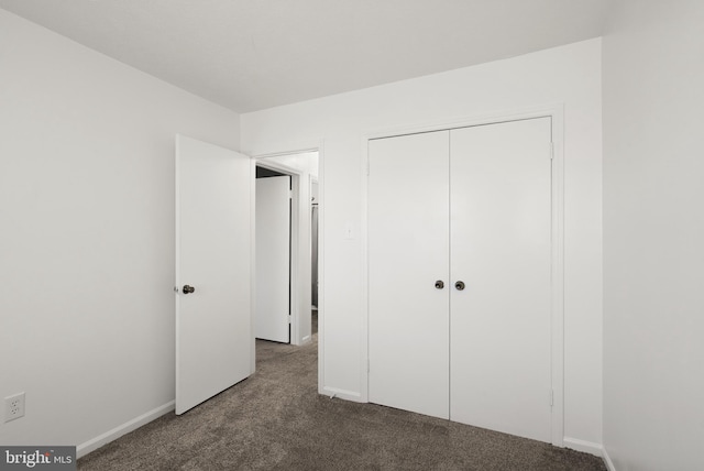 unfurnished bedroom with baseboards, dark carpet, and a closet