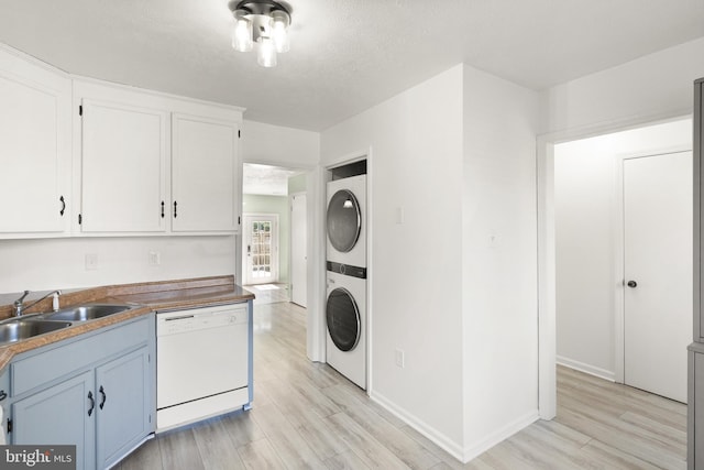 washroom featuring laundry area, stacked washer / drying machine, a sink, baseboards, and light wood-style flooring