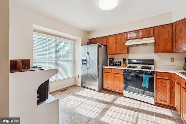 10048 Quiet Brook Ln, Clinton, MD 20735 - kitchen with brown cabinets, under cabinet range hood, gas range, light countertops, and stainless steel fridge with ice dispenser