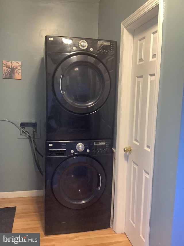 clothes washing area with baseboards, laundry area, wood finished floors, and stacked washer / dryer