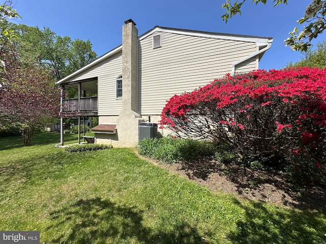 view of side of property featuring a lawn, a chimney, and cooling unit