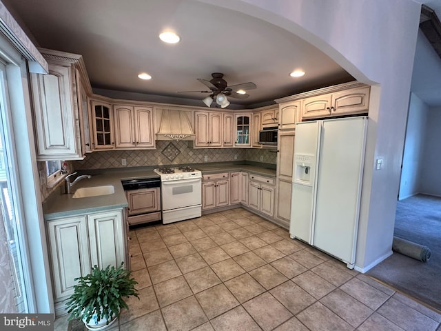 kitchen with white appliances, arched walkways, custom range hood, a sink, and backsplash