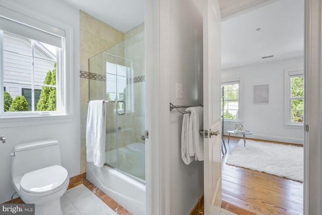 full bath featuring baseboards, combined bath / shower with glass door, and toilet