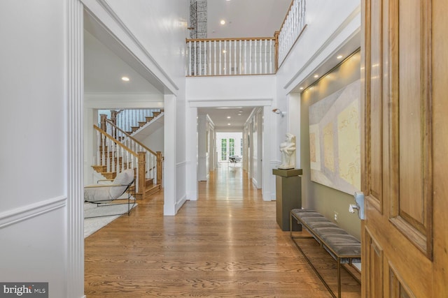foyer entrance featuring a towering ceiling, wood finished floors, stairway, baseboards, and ornamental molding