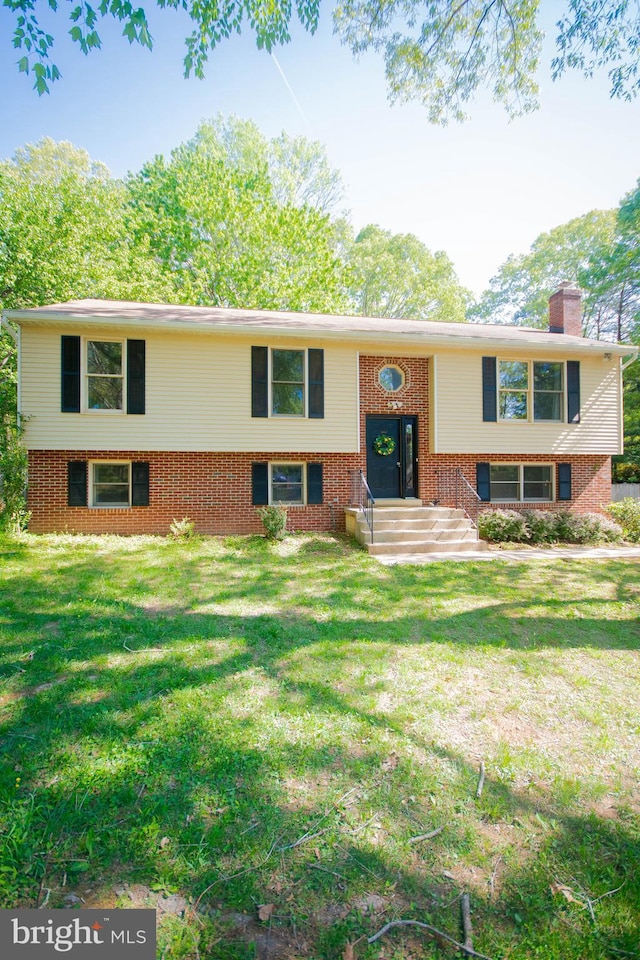 raised ranch with brick siding, a front lawn, and a chimney
