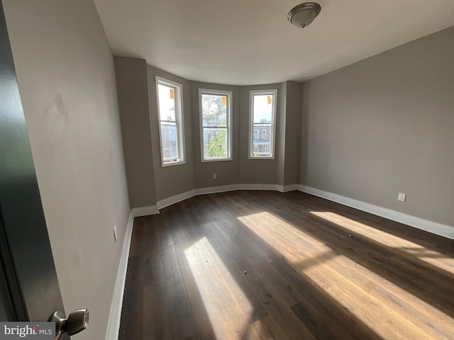 empty room with baseboards and dark wood-type flooring