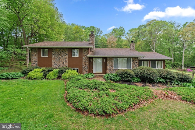 split level home featuring stone siding, fence, a chimney, and a front lawn