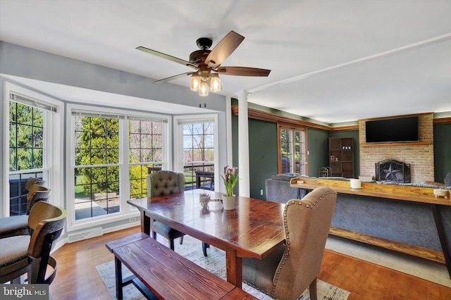 dining room featuring a brick fireplace, ceiling fan, plenty of natural light, and wood finished floors