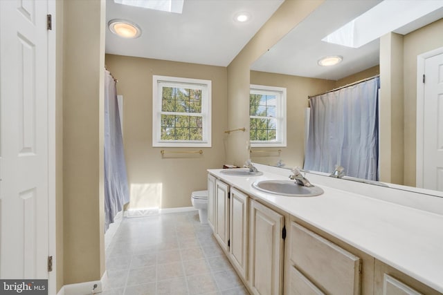 full bath with baseboards, double vanity, a skylight, and a sink