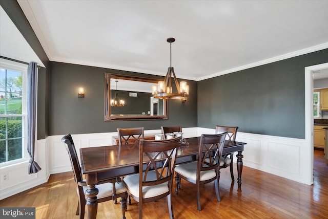 dining area featuring crown molding, an inviting chandelier, wainscoting, a decorative wall, and wood finished floors