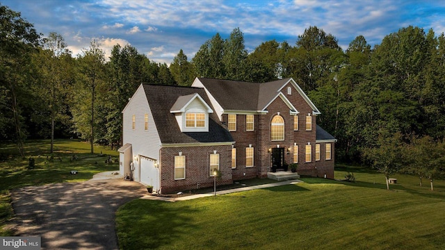 view of front of home with driveway, an attached garage, brick siding, a front yard, and a forest view