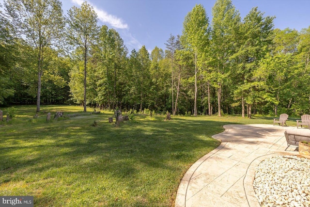 view of green lawn featuring a patio and a forest view