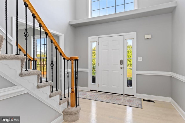 foyer entrance with healthy amount of natural light, wood finished floors, baseboards, and a high ceiling