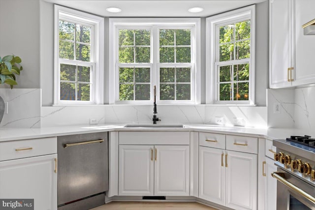 kitchen featuring a sink, tasteful backsplash, stainless steel appliances, white cabinetry, and light stone counters