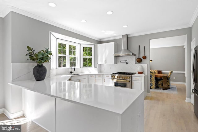 kitchen with wall chimney exhaust hood, high end stainless steel range oven, a sink, a peninsula, and white cabinets