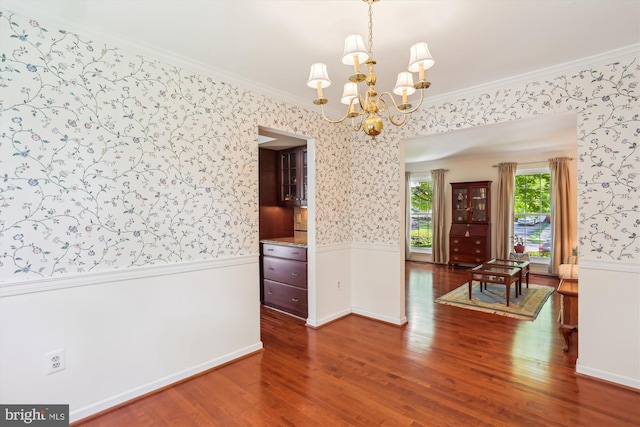 unfurnished dining area featuring an inviting chandelier, wood finished floors, a wainscoted wall, and wallpapered walls