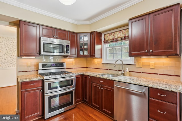 kitchen featuring dark wood-style flooring, a sink, light stone counters, ornamental molding, and stainless steel appliances