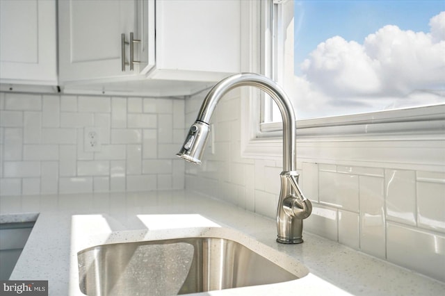 room details with a sink, light stone counters, backsplash, and white cabinetry