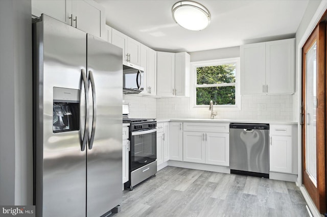 kitchen featuring light wood-style floors, white cabinets, tasteful backsplash, a sink, and stainless steel appliances