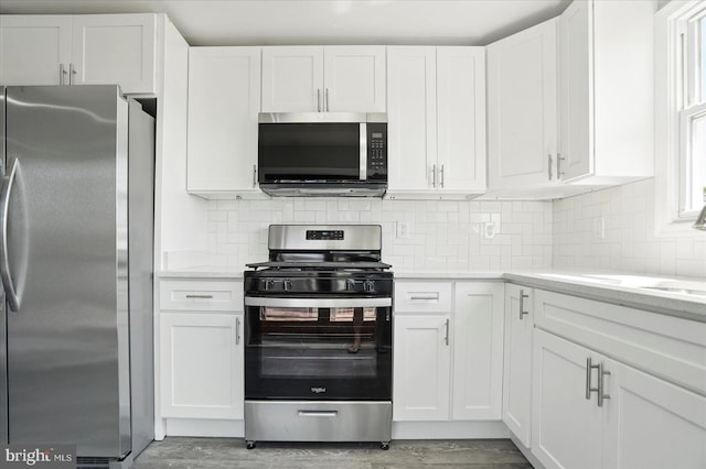 kitchen with white cabinets, a sink, light wood-style floors, stainless steel appliances, and tasteful backsplash