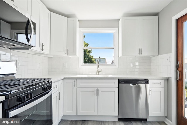 kitchen with appliances with stainless steel finishes, a sink, light countertops, white cabinetry, and backsplash