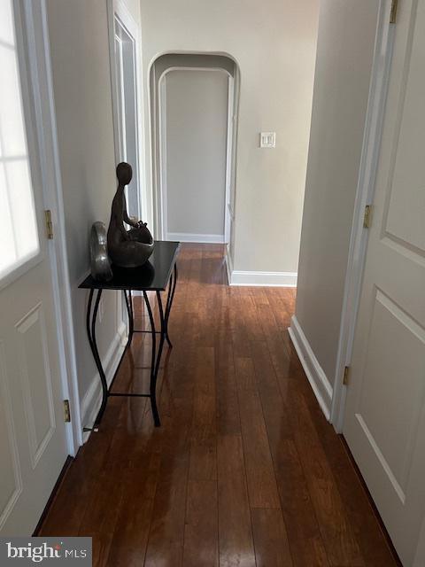 hall featuring arched walkways, baseboards, and hardwood / wood-style flooring