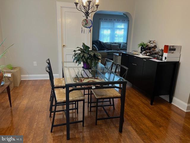 dining space with arched walkways, baseboards, an inviting chandelier, and wood finished floors