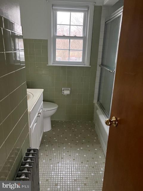 full bathroom with tile patterned flooring, vanity, toilet, radiator, and tile walls