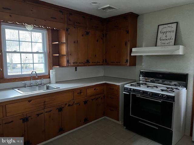 kitchen with visible vents, a sink, light countertops, under cabinet range hood, and gas range oven