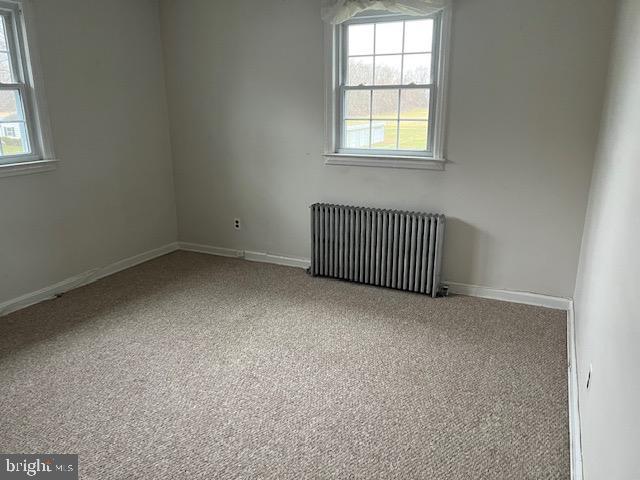 spare room with plenty of natural light, baseboards, carpet, and radiator heating unit