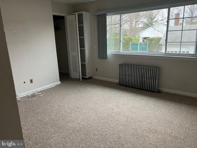 unfurnished bedroom featuring radiator heating unit, carpet floors, baseboards, and a closet