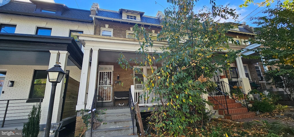 view of front facade with roof with shingles, a porch, mansard roof, and brick siding