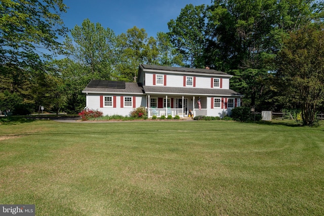 colonial home with roof mounted solar panels, covered porch, a chimney, and a front lawn