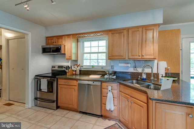 kitchen with a sink, dark stone countertops, appliances with stainless steel finishes, and backsplash