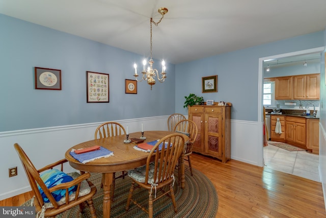 dining space with a wainscoted wall, light wood-type flooring, and a chandelier