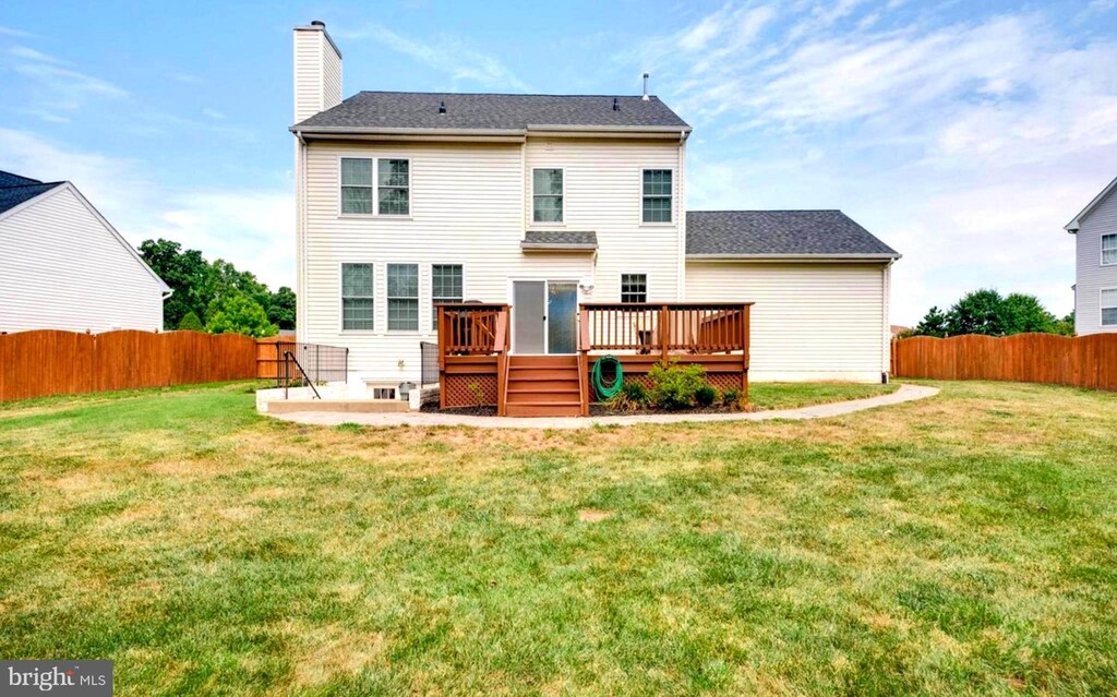 back of house with a lawn, a deck, a chimney, and a fenced backyard