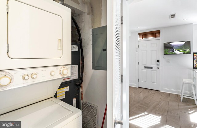 clothes washing area with laundry area, stacked washing maching and dryer, baseboards, visible vents, and electric panel