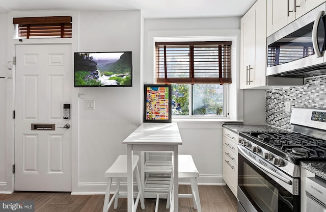 kitchen featuring tasteful backsplash, wood finished floors, baseboards, white cabinets, and stainless steel appliances