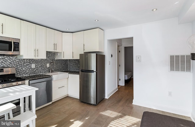 kitchen with appliances with stainless steel finishes, tasteful backsplash, wood finished floors, a sink, and white cabinetry