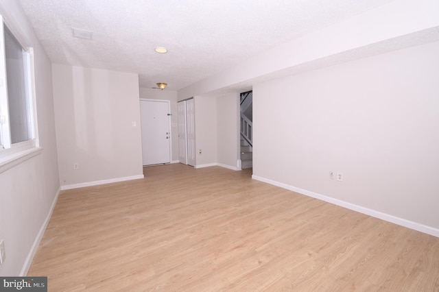unfurnished room featuring baseboards, light wood finished floors, stairs, and a textured ceiling