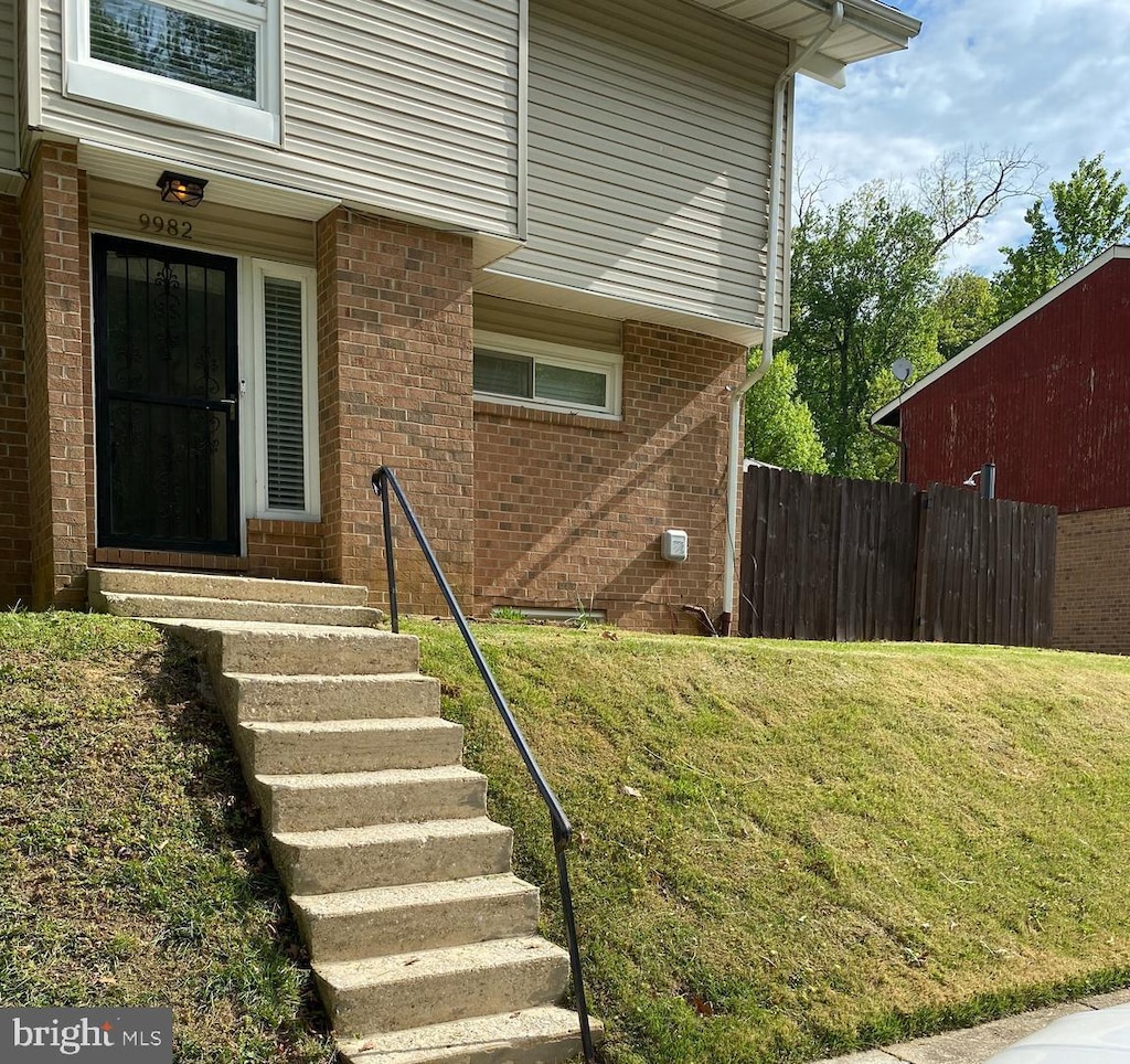 property entrance featuring brick siding, fence, and a yard