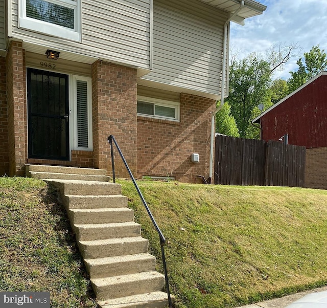 property entrance featuring brick siding, fence, and a yard