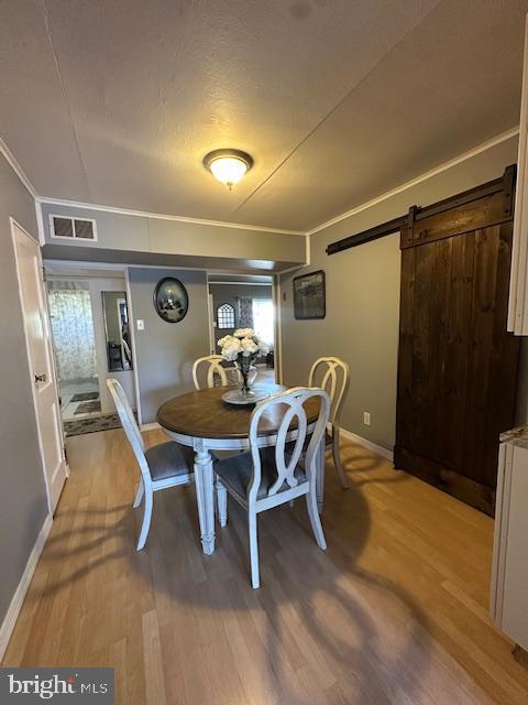 dining space with visible vents, ornamental molding, wood finished floors, baseboards, and a barn door