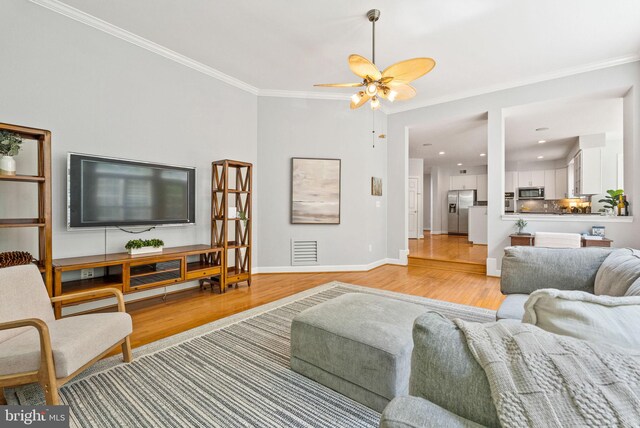 living room featuring visible vents, ornamental molding, light wood-style flooring, and a ceiling fan